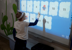 Chłopiec na tablicy multimedialnej gra w memory misiowe.