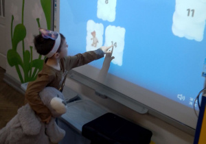 Chłopiec stoi przed tablicą multimedialną i gra w memory misiowe.