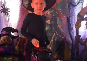 Chłopiec w czarnym kapeluszu na głowie losuje z czarnego kociołka ciasteczkową wróżbę.