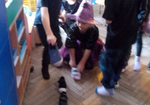 Przedszkolaki stoją w rozsypce, obok ustawione buty w rzędzie, przy których kucają dziewczynki.