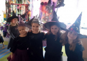 Grupka dziewczynek w kapeluszach na głowie pozują na tle dekoracji.