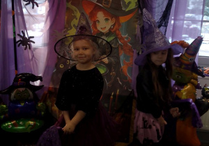 Dwie dziewczynki w kapeluszach na głowie pozują do zdjęcia na tle dekoracji z miotłami.