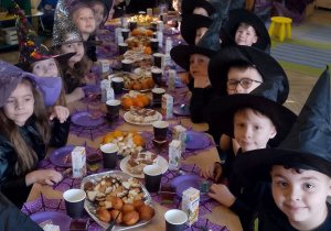 Dzieci siedzą przy złączonych stołach podczas andrzejkowego poczęstunku.