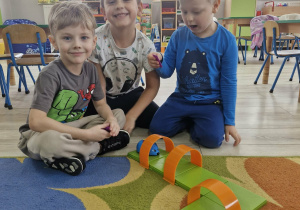 Olek, Franek i Karol siedzą na dywanie. Przed chłopcami leży zestaw do kodowania z myszką.