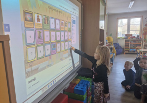 Ala w trakcie losowania wróżby stoi przy tablicy multimedialnej.