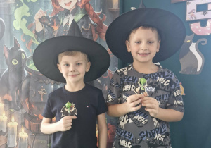 Olek i Franek w kapeluszach wiedźmy pozują do zdjęcia na tle andrzejkowej dekoracji.