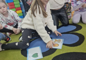 Oliwka siedząc na dywanie dopasowuje obrazki z misiami.