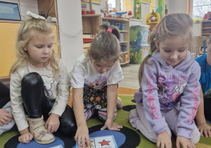 Ala, Klara i Zuzia siedzą na dywanie i układają obrazki z misiami.