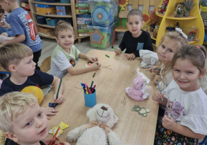 Przedszkolaki siedzą przy stoliku i kolorują flamastrami drewniane misie.