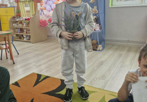 Olek troi na tle dekoracji i trzyma w dłoniach kwiatek. Przed chłopcem leży obrazek z wizerunkiem misia trzymającego kwiatek.