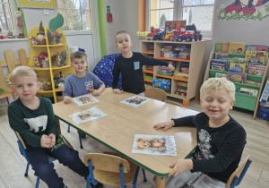 Lucjan, Staś, Wojtuś i Karolek siedzą przy stoliku. Przed chłopcami leżą ułożone z części obrazki z wizerunkami misiów.