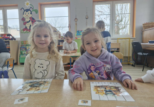 Ala i Zuzia siedzą przy stoliku. Przed dziewczynkami leżą ułożone z części obrazki z wizerunkami misiów.