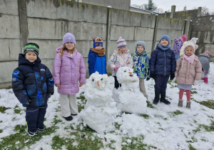 Dzieci pozują do zdjęcia ze śniegowymi bałwankami.