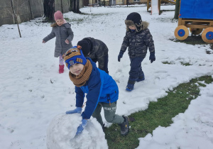 Marcel toczy przed sobą dużą śniegową kulę potrzebną do ulepienia bałwana.