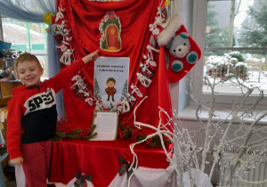 Oliwier stoi obok tablicy i pokazuje przypięte obok kalendarza adwentowego magiczne drzwi.