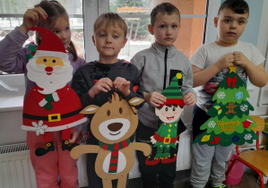 Czworo dzieci stoi obok siebie trzymając ozdoby z filcu: Mikołaja, renifera, Elfa, choinkę.