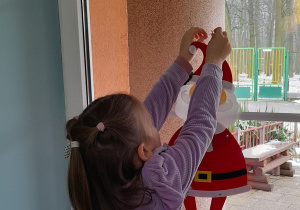 Weronika wiesza Mikołaja na oknie.