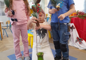 Troje dzieci wkłada do wazonu świąteczne gałązki.