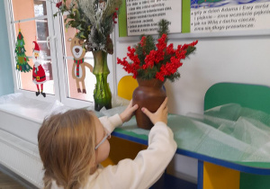 Zuzia ustawia wazon z gałązkami świątecznymi w kąciku przyrody.