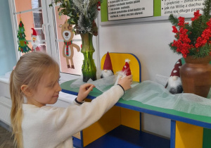 Nikola ustawia figurki Mikołajów obok wazonów, w których znajdują się świąteczne gałązki.