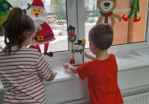 Nadia i Jakub stawiają bałwanka i Mikołaja na parapecie.