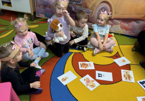 Dzieci siedzą na dywanie. Na głowach mają opaski z misiami.