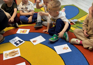 Chłopcy siedzą na dywanie z opaskami misiów na głowach. Na dywanie są ilustracje z małymi i dużymi misiami.