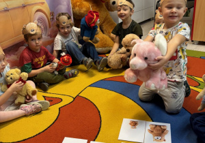 Chłopcy siedzą na dywanie z opaskami misiów na głowach. Na dywanie są ilustracje z małymi i dużymi misiami.