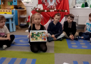 "Słoneczka" siedzą na dywanie, a Tosia prezentuje kolejny obrazek.