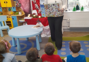 Pani z biblioteki prezentuje dzieciom przyniesioną książkę.