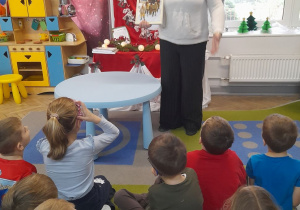 Dzieci siedzą na dywanie, a Pani prezentuje koleją książkę o tematyce świątecznej.