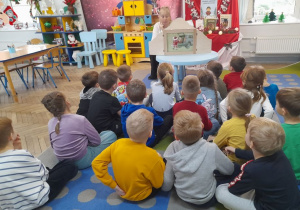 Dzieci siedzą na dywanie, a Pani czyta bajkę zaprezentowaną w Teatrzyku Kamishibai.