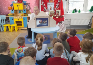 Dzieci siedzą na dywanie i słuchają kolejnego fragmentu bajki zaprezentowanej w Teatrzyku Kamishibai.