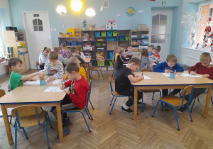 Dzieci siedzą przy stołach i wykonują rysunkowe listy do Świętego Mikołaja.