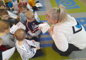 Dzieci siedzą na dywanie trzymając listy do Świętego Mikołaja, a przed nimi przykucnęła Pani z biblioteki. Fabian opowiada co narysował w swoim liście.