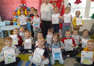 Dzieci pozują do zdjęcia razem z zaproszonym gościem. Przedszkolaki trzymają przed sobą rysunkowe listy do Świętego Mikołaja.