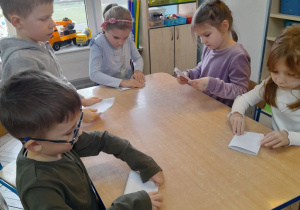 Pięcioro dzieci siedzi przy stole i składa swoje listy do Świętego Mikołaja.