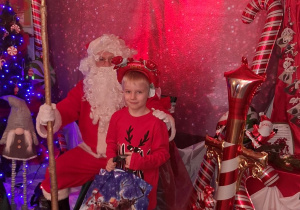 Fabian na tle dekoracji pozuje do zdjęcia z Mikołajem.