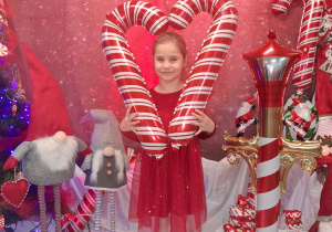 Marysia pozuje do zdjęcia z biało-czerwonymi balonowymi laskami. W tle dekoracja.