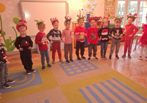 Dzieci w mikołajkowych opaskach ustawione w półkolu śpiewają piosenkę.