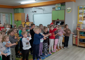 Dzieci stoją poruszając rękami, a przed nimi Pan prowadzący zajęcia. Wszyscy bawią się przy piosence.