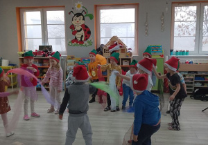 Dzieci w czapkach świątecznych razem z Panem prowadzącym zajęcia bawią się chustkami przy dźwiękach klarnetu.