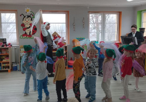 Pan gra na klarnecie, a grupka dzieci porusza się w kole wymachując chustkami.