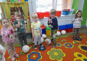 Grupka dzieci stoi na dywanie między piłkami.