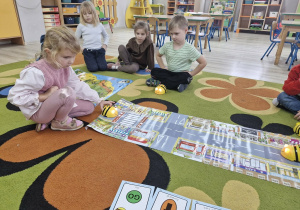 Alicja programuje Bee Bota. Przed matą leżą karty do kodowania według których dziewczynka koduje pszczółkę. Wokół siedzą inne dzieci z grupy.