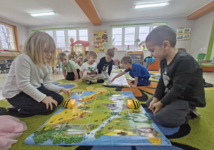 Nadia i Wojtuś siedzą naprzeciwko siebie i programują pszczółki Bee Bot na macie do kodowania "mapa skarbów".