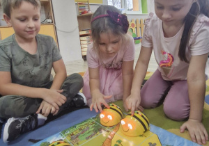Franuś, Klara i Oliwka siedzą wokół maty do kodowania "mapa skarbów" i programują Bee Boty.