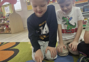 Julek siedzi przed matą do kodowania przedstawiającą drogę. Chłopiec programuje Bee Bota. Obok poczynaniom Julka przygląda się Oluś.