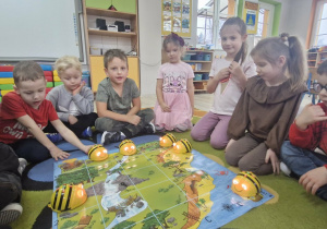 Dzieci siedzą zebrane wokół maty do kodowania przedstawiającej mapę skarbów. Na macie widać rozłożone interaktywne pszczółki Bee Bot.