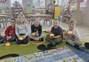 Antek, Nadia, Julek, Szymek i Olek siedzą przed matą do kodowania. Dzieci trzymają w dłoniach interaktywne pszczółki Bee Bot.